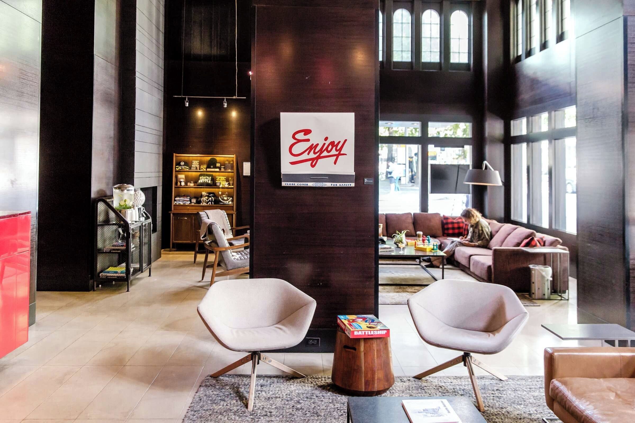 A modern interior with a central column featuring a 'Enjoy' sign, seating areas, and a visible storefront.