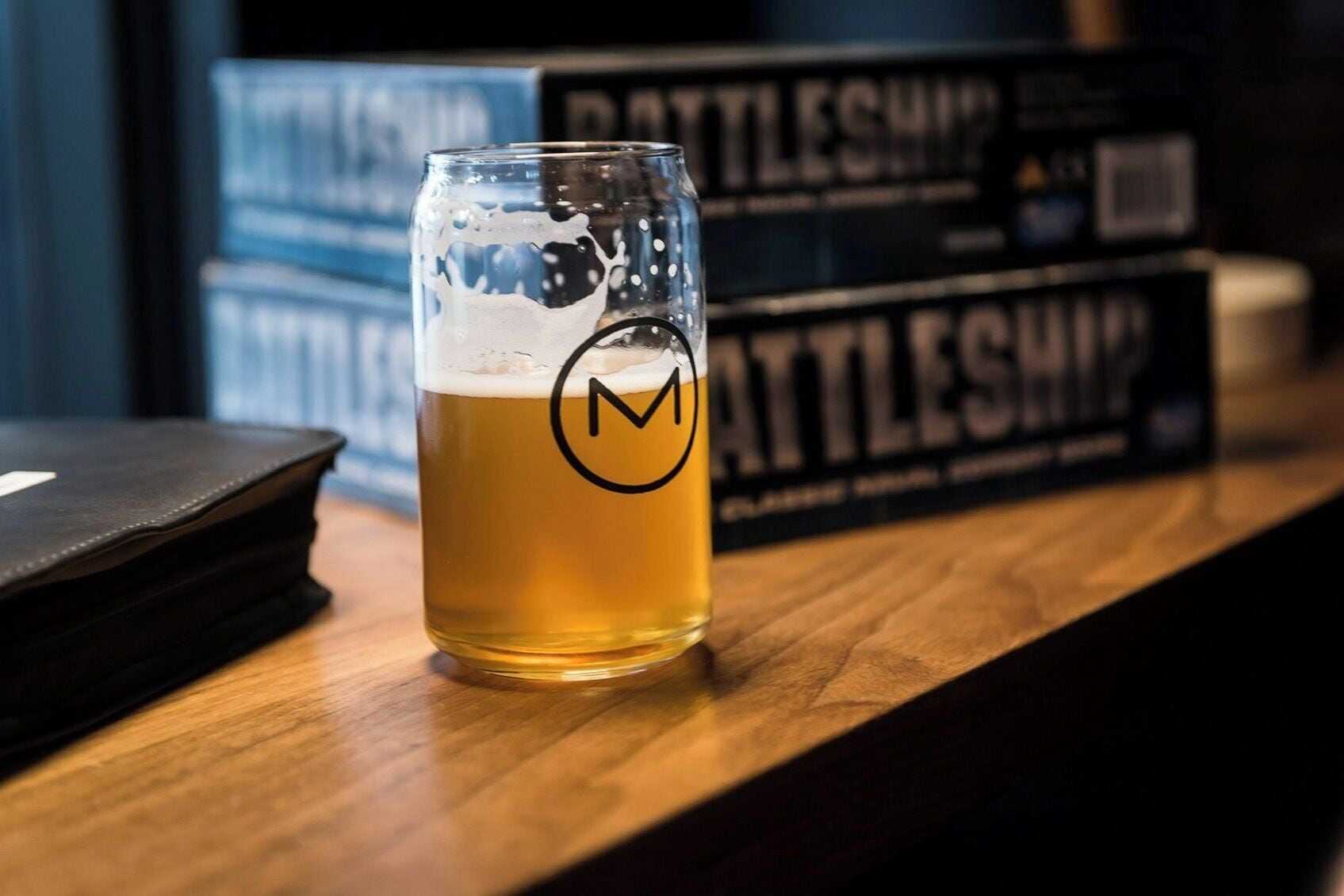 Un verre de bière posé sur une surface en bois, avec des livres en arrière-plan.