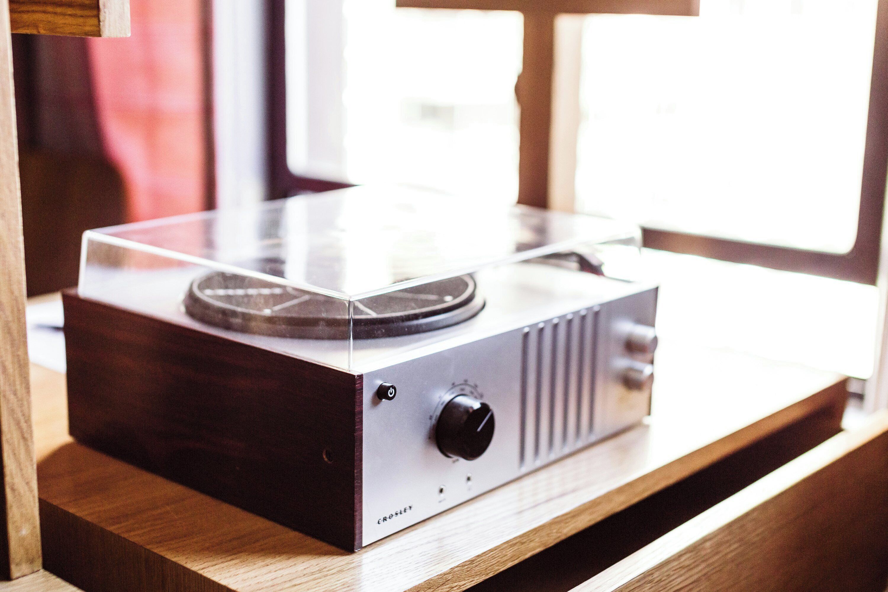 Tocadiscos sobre una superficie de madera con una ventana al fondo.