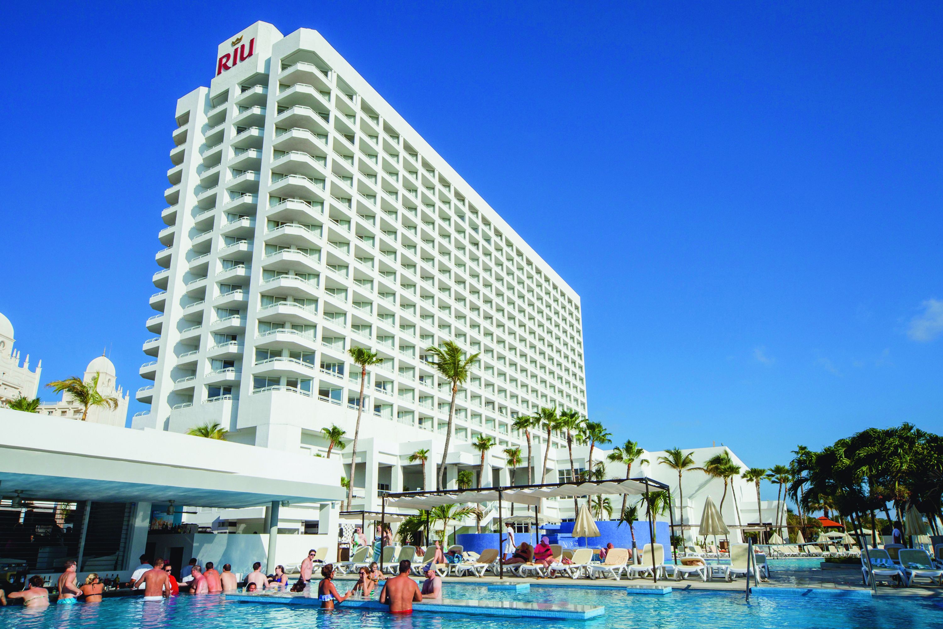 Un grand hôtel doté d’une piscine, de palmiers et surplombant un ciel d’un bleu limpide.
