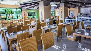A spacious restaurant with wicker chairs and tables, large windows, and a high ceiling with exposed beams.