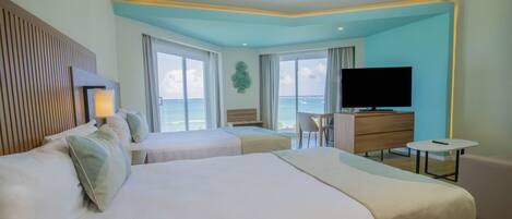 A hotel room with two beds, a TV, a desk, and a view of the ocean.