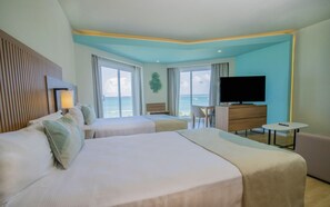 A hotel room with two beds, a TV, a desk, and a view of the ocean.