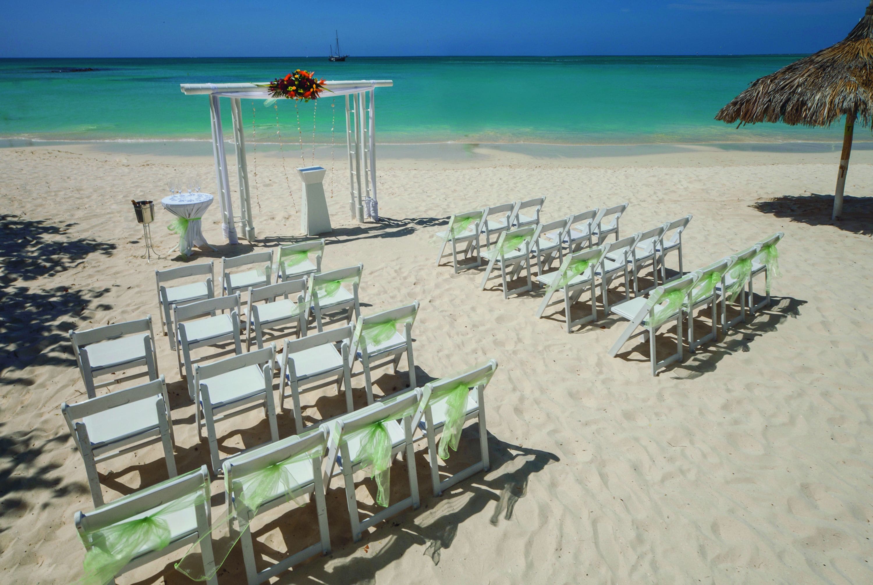A beach wedding setup with white chairs and a white arch.
