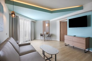 A modern living room with a sofa, a coffee table, a TV, and a dining area with chairs and a table.