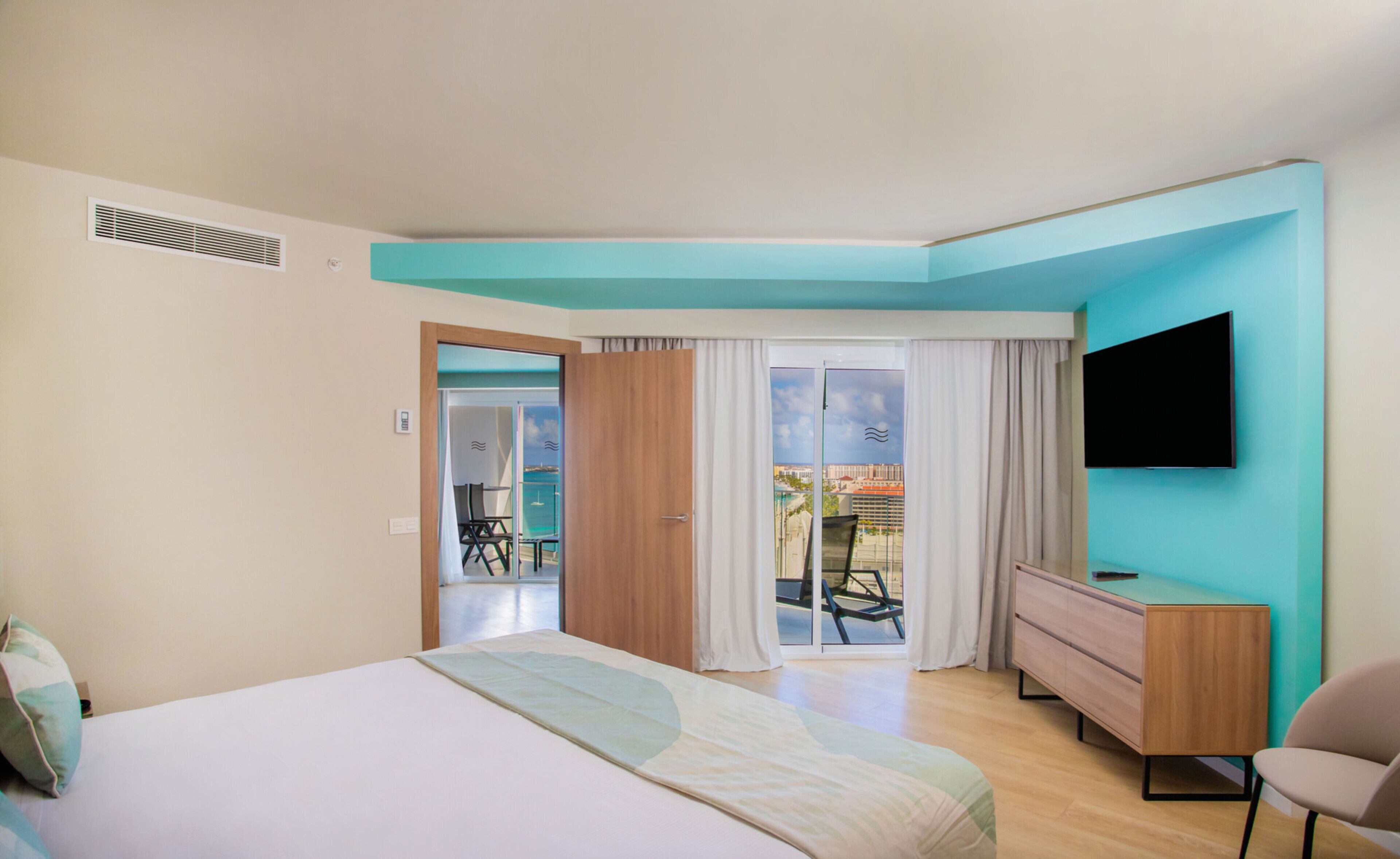 Une chambre d’hôtel moderne équipée d’un lit, d’une télévision, d’une commode et d’un balcon avec vue.