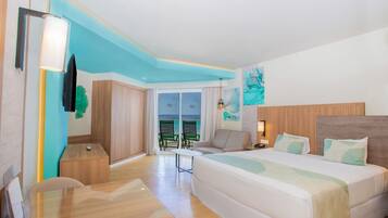 A hotel room with a bed, a desk, a chair, a TV, and a view of the sea.
