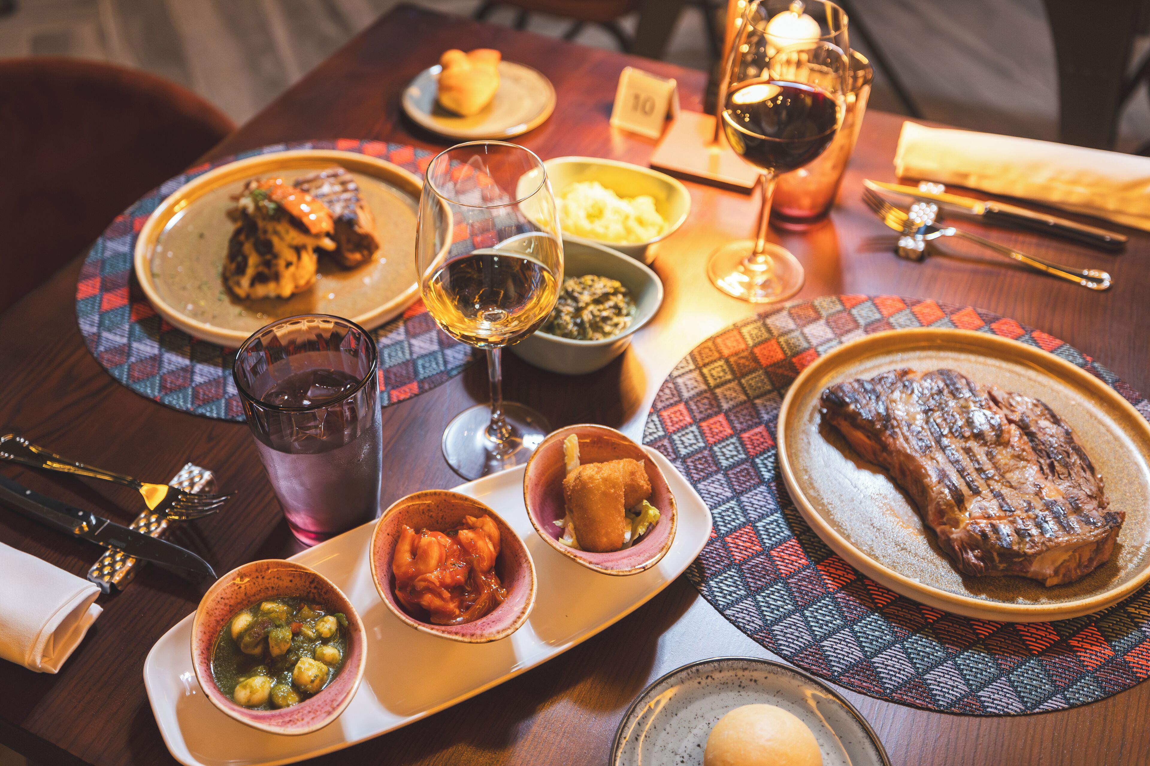 A dining table set with various dishes, including a steak, a bowl of soup, and a glass of wine.