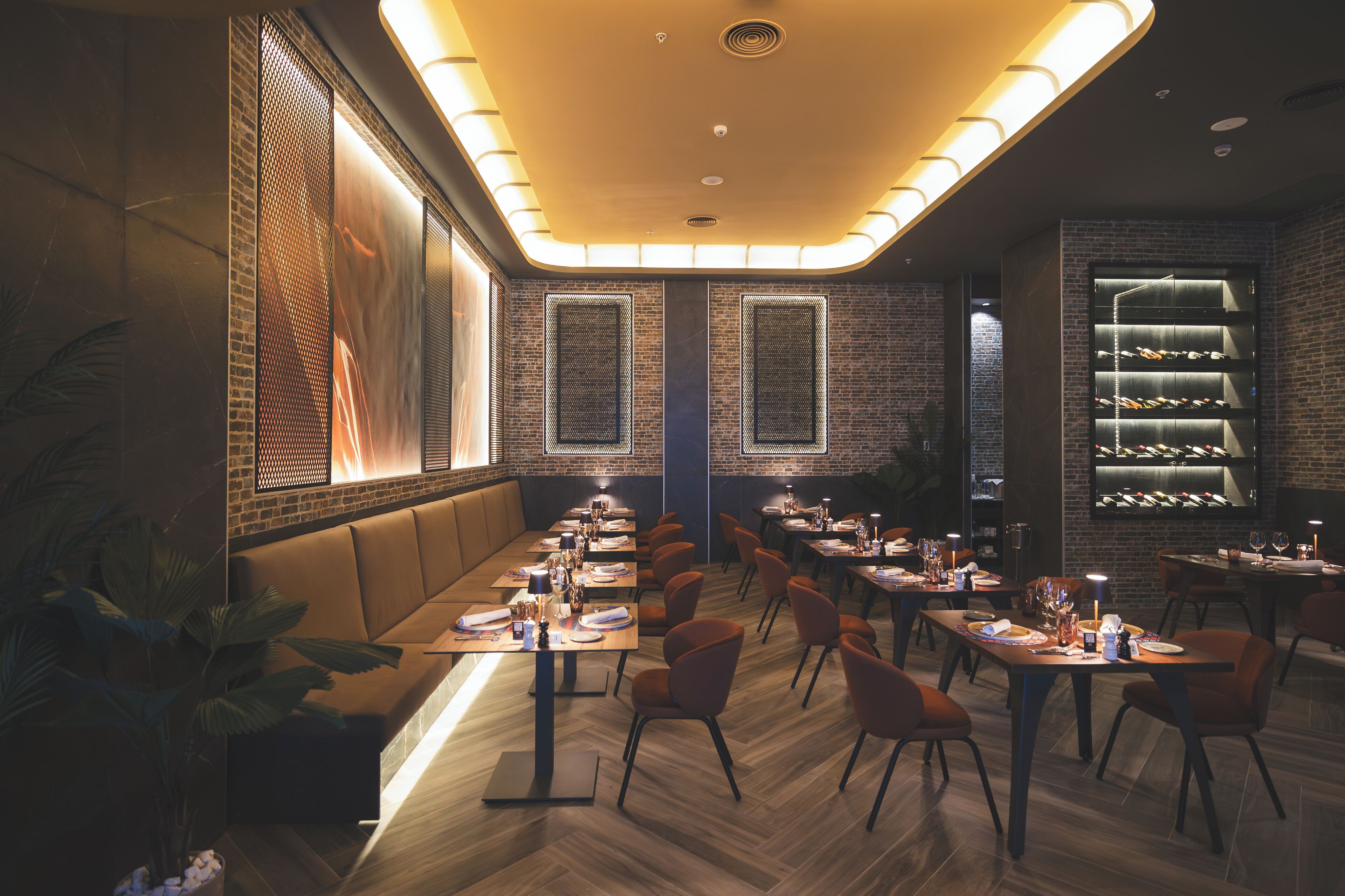 Un restaurant doté d’un long comptoir, de plusieurs tables et de chaises. On peut y voir des plantes et un présentoir à bouteilles de vin.