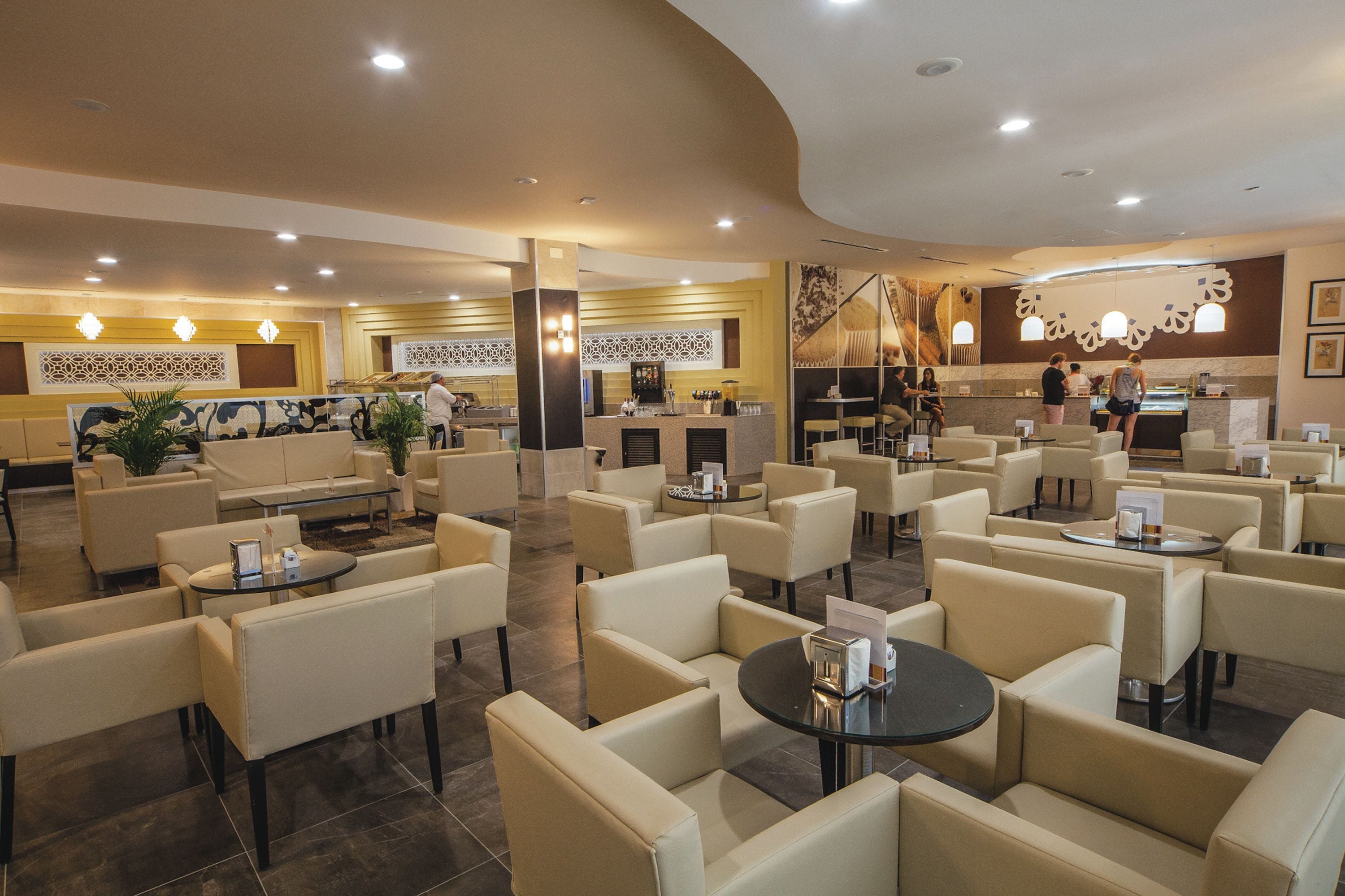 Un hall d’hôtel spacieux, doté de plusieurs espaces de détente, d’un comptoir d’accueil et d’un bar.