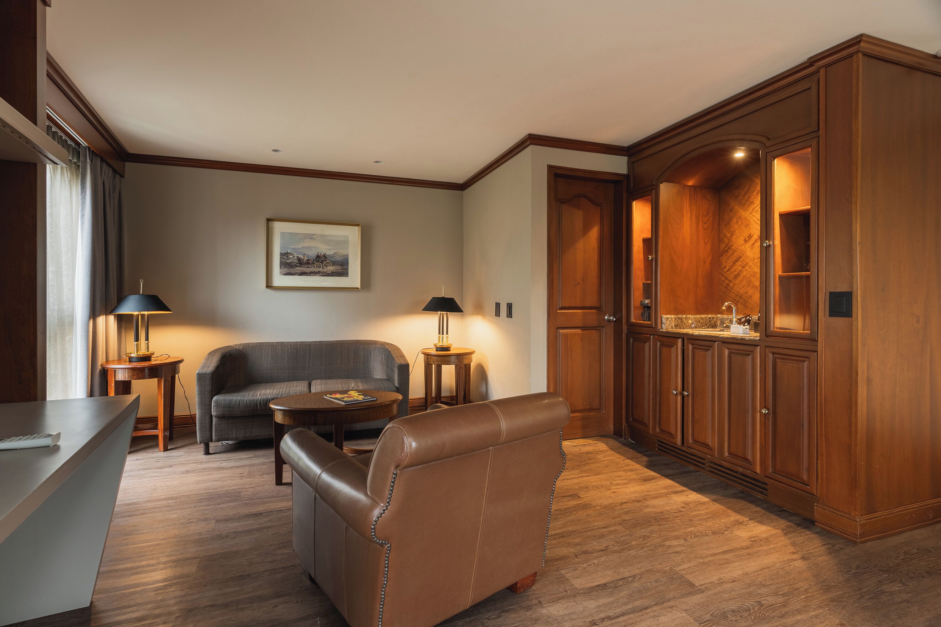 A room with a sofa, a chair, a small table, a lamp, and wooden cabinets.