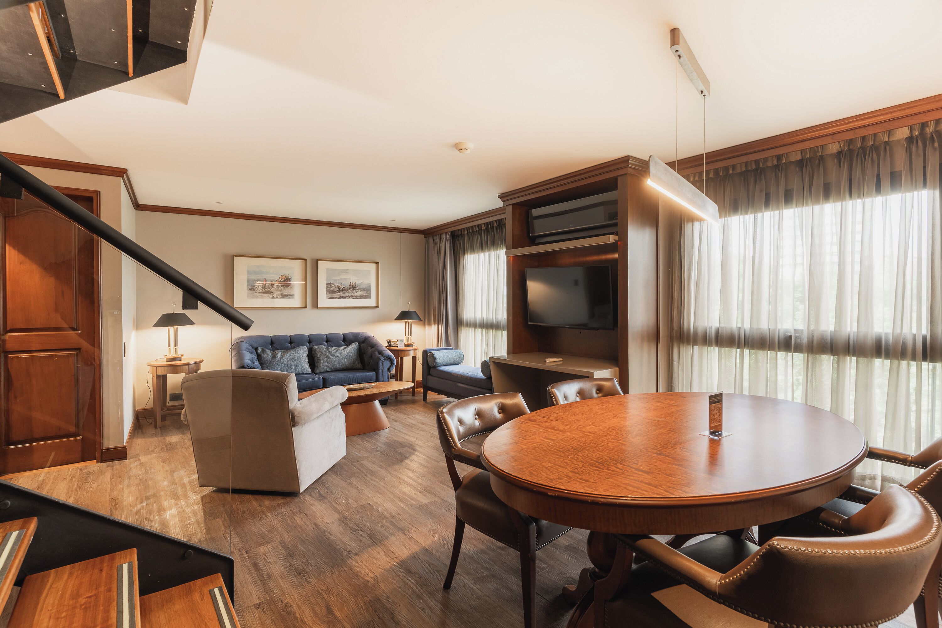 A modern living room with a round wooden table, leather chairs, a sofa, and a television.