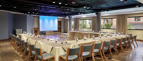 A conference room with multiple tables, chairs, and a large screen for presentations.