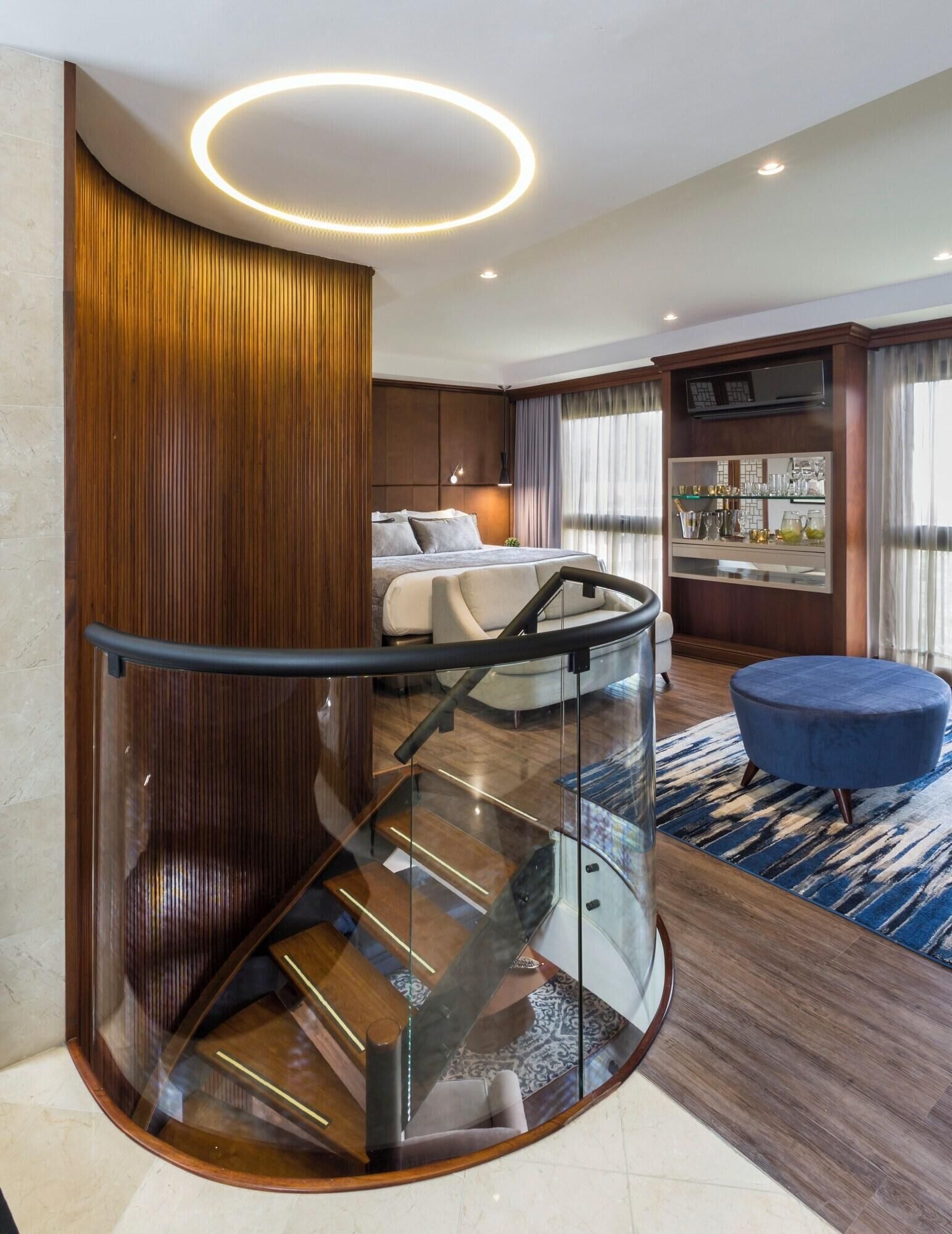 Una habitación de hotel moderna con una escalera curva, una cama, una zona de estar y un bar.