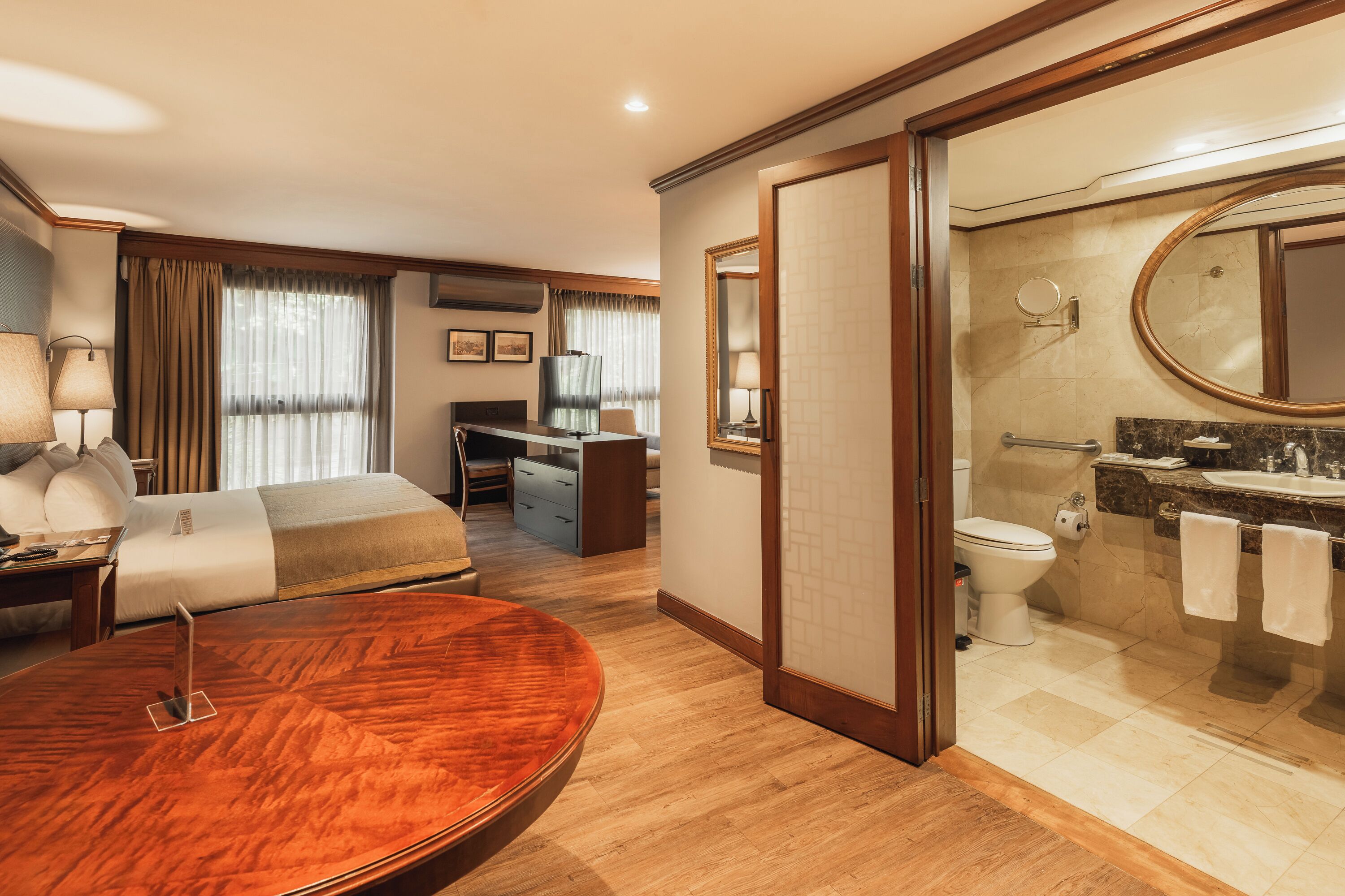 Habitación de hotel con cama, escritorio, silla y una mesa redonda de madera.