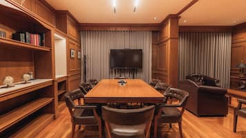 A conference room with a wooden table, leather chairs, a flat-screen TV, and a bookshelf.
