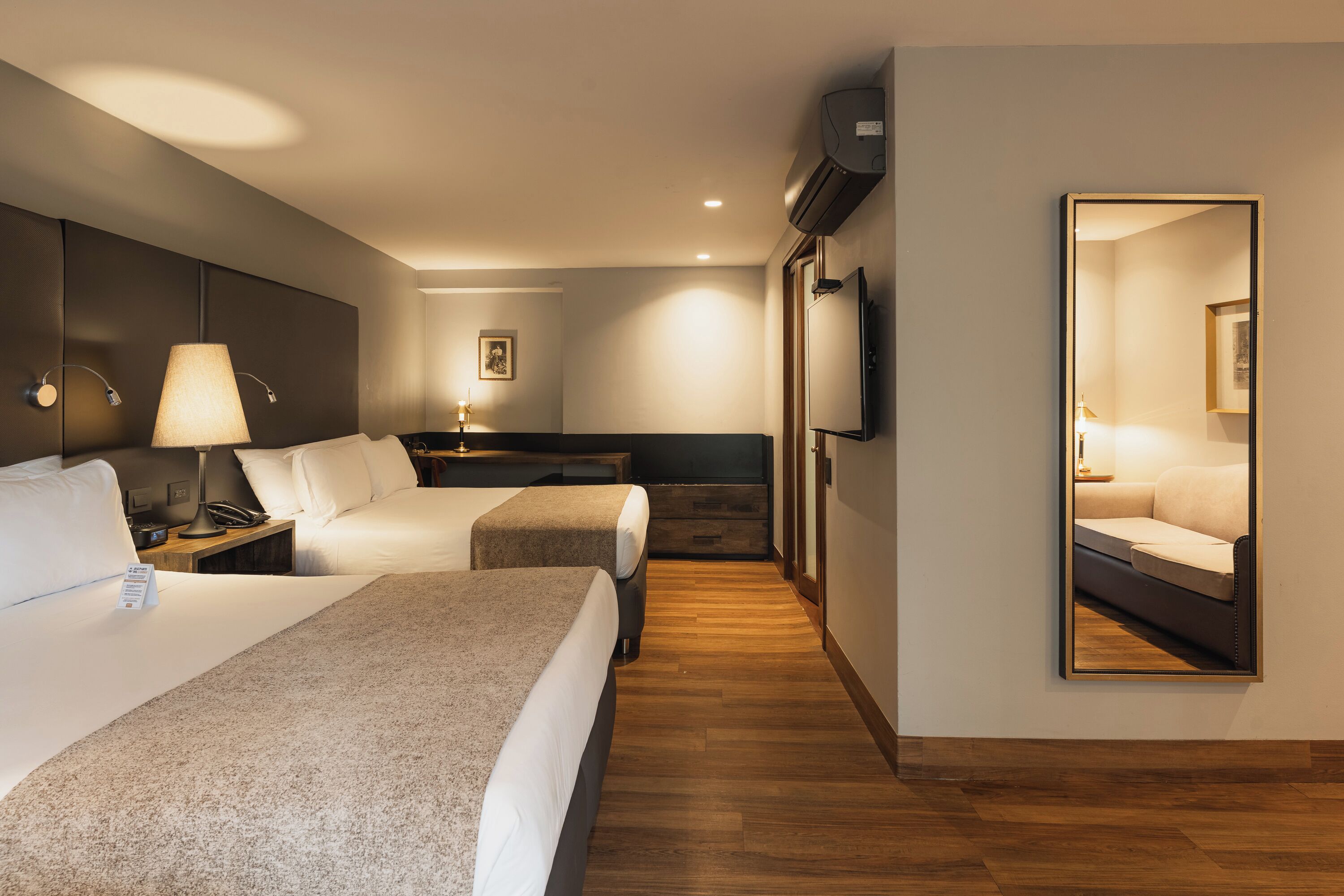 A hotel room with two beds, a desk, a chair, a TV, and a large mirror.