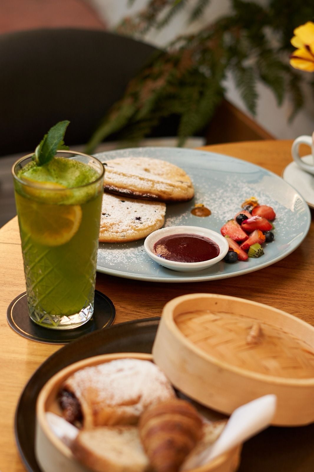 A breakfast setting with a plate of pastries, a glass of green drink, and a small bowl of jam.