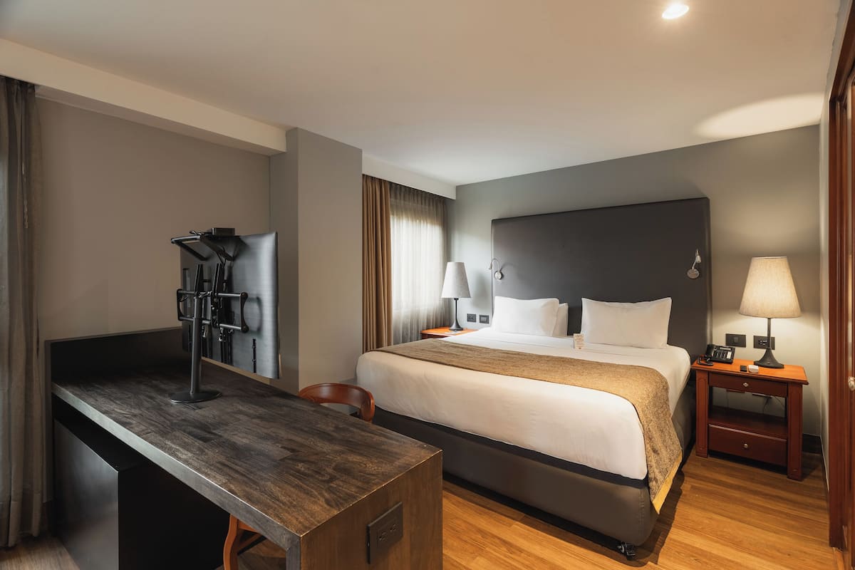 A hotel room with a bed, bedside tables, a desk, and a chair.