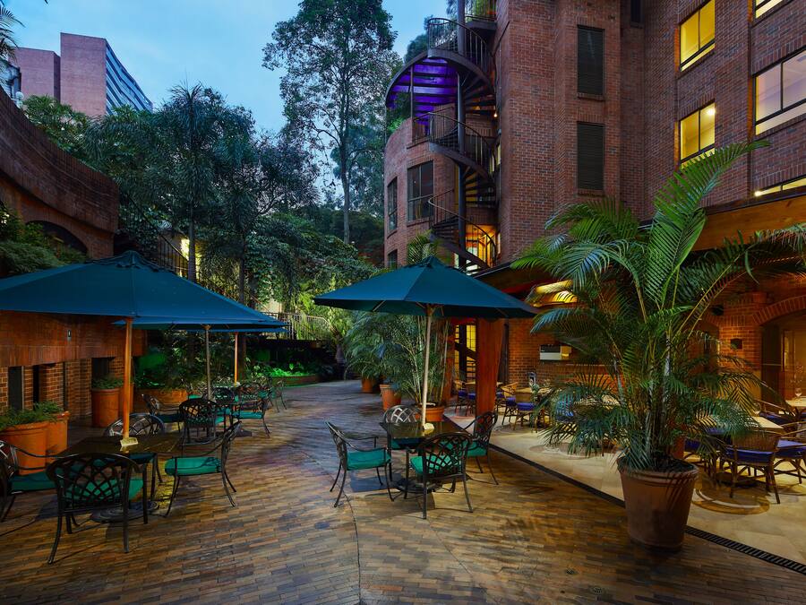 Un patio al aire libre con suelo de ladrillo, mobiliario exterior con sombrillas y plantas en macetas.