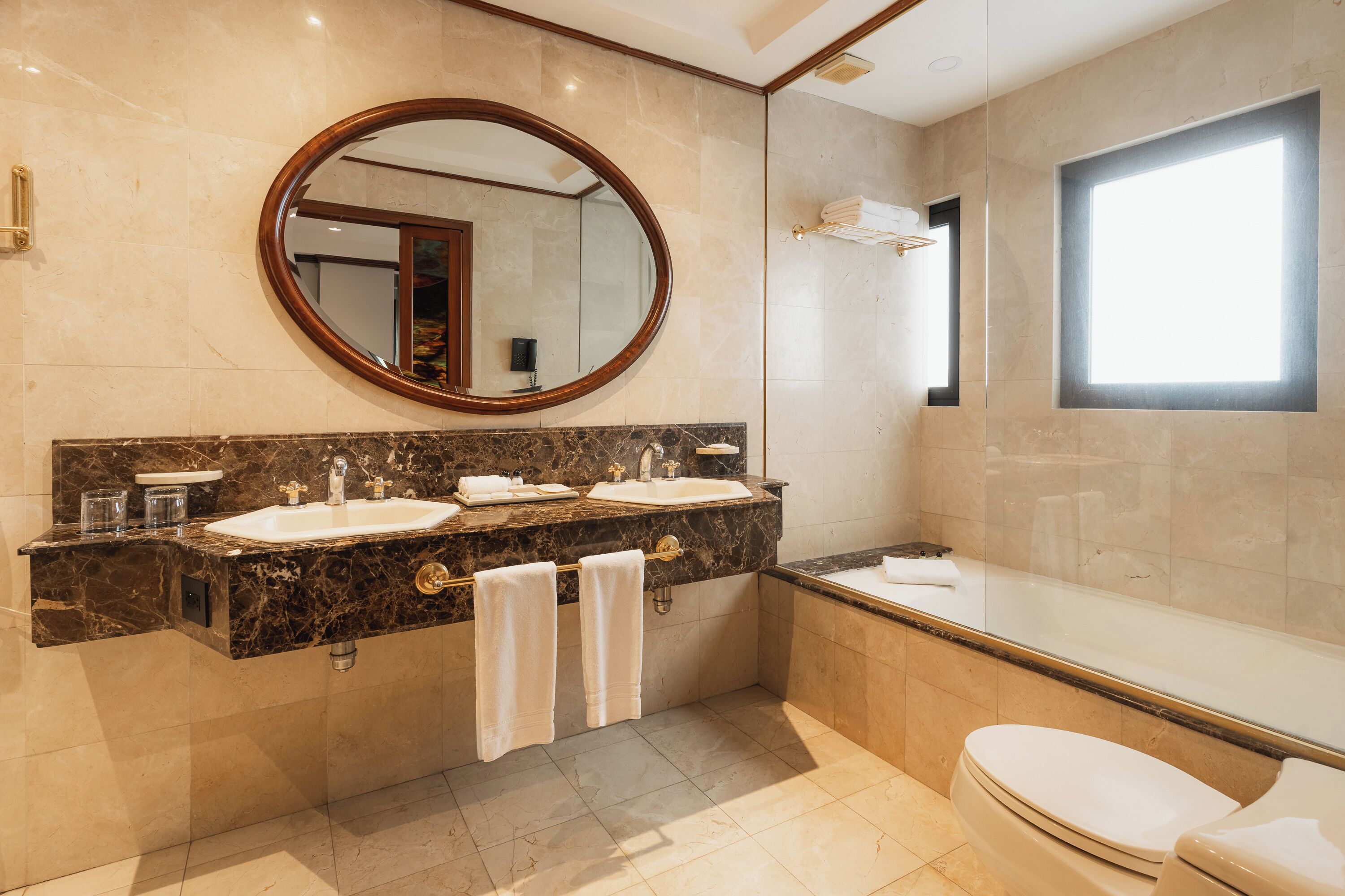 Un baño moderno con un espejo ovalado grande, lavamanos dobles, bañera y retrete.