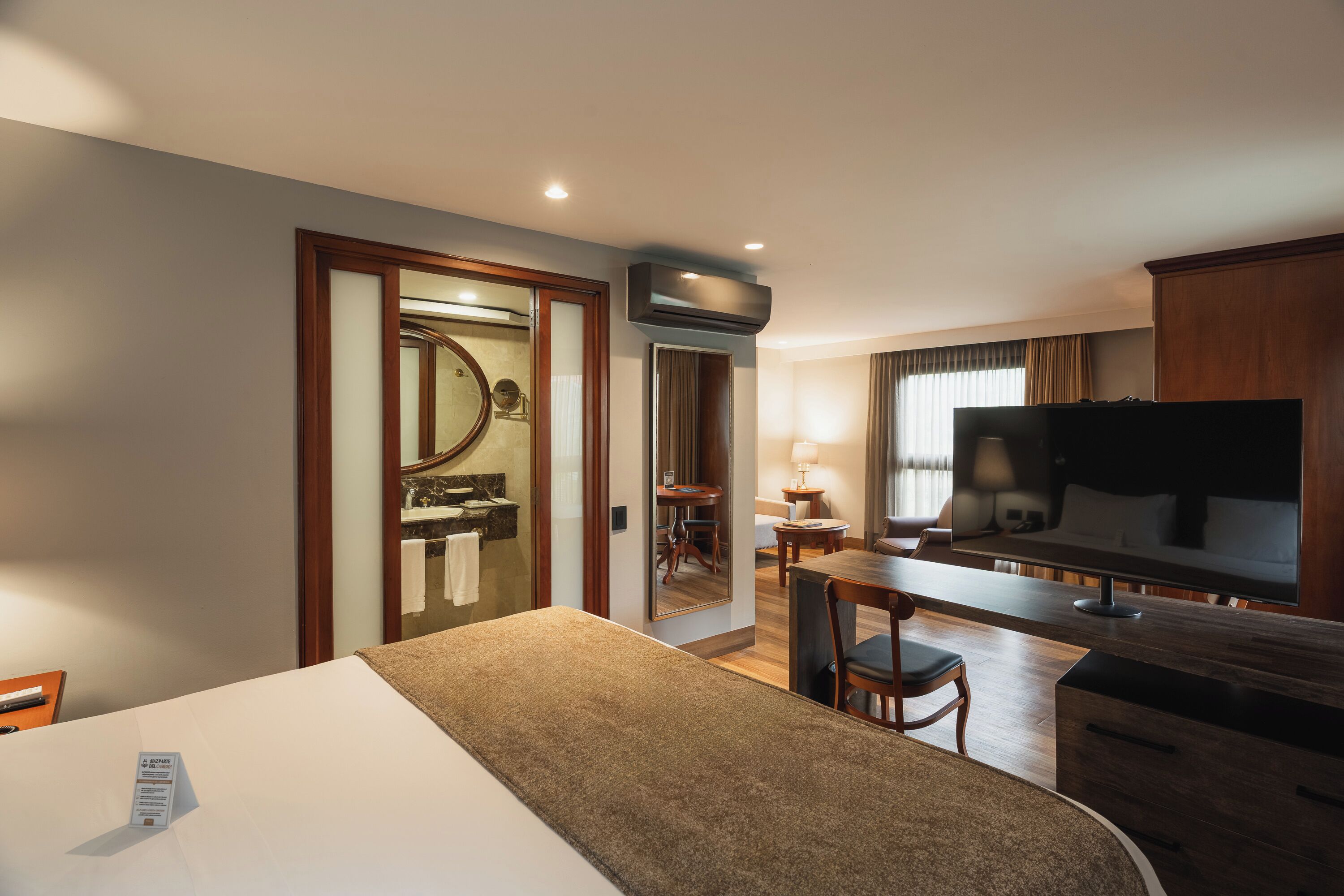 Hotelkamer met een bed, een bureau, een televisietoestel, een spiegel en een badkamer die door een open deur zichtbaar is.