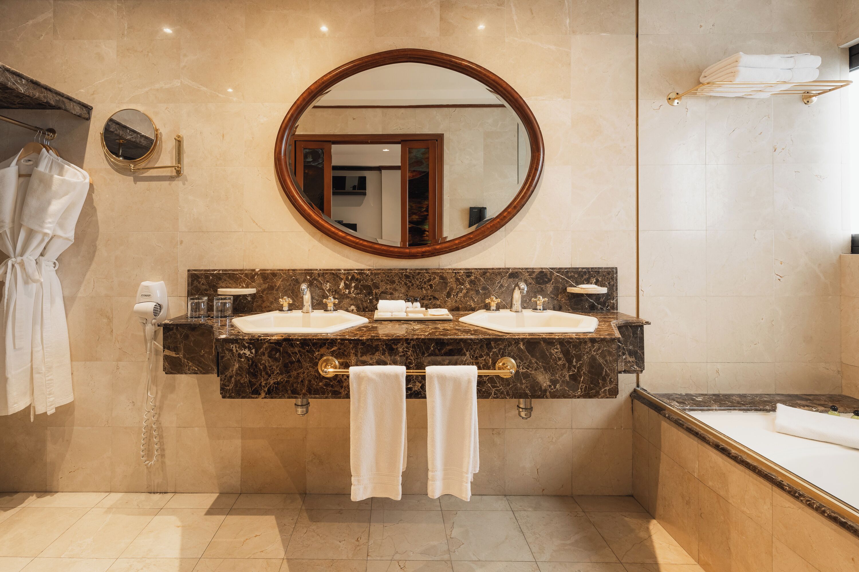 Un baño con dos lavamanos, un espejo grande, un perchero para toallas y una bañera.