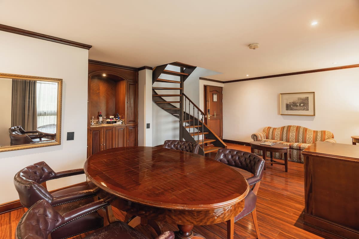 A conference room with a wooden table, leather chairs, a staircase, a sofa, and a framed picture on the wall.