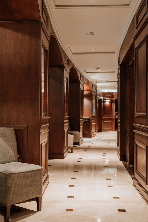 A hallway with wooden paneling, a chair, and a polished marble floor. - Hotel Park 10 (Medellín)