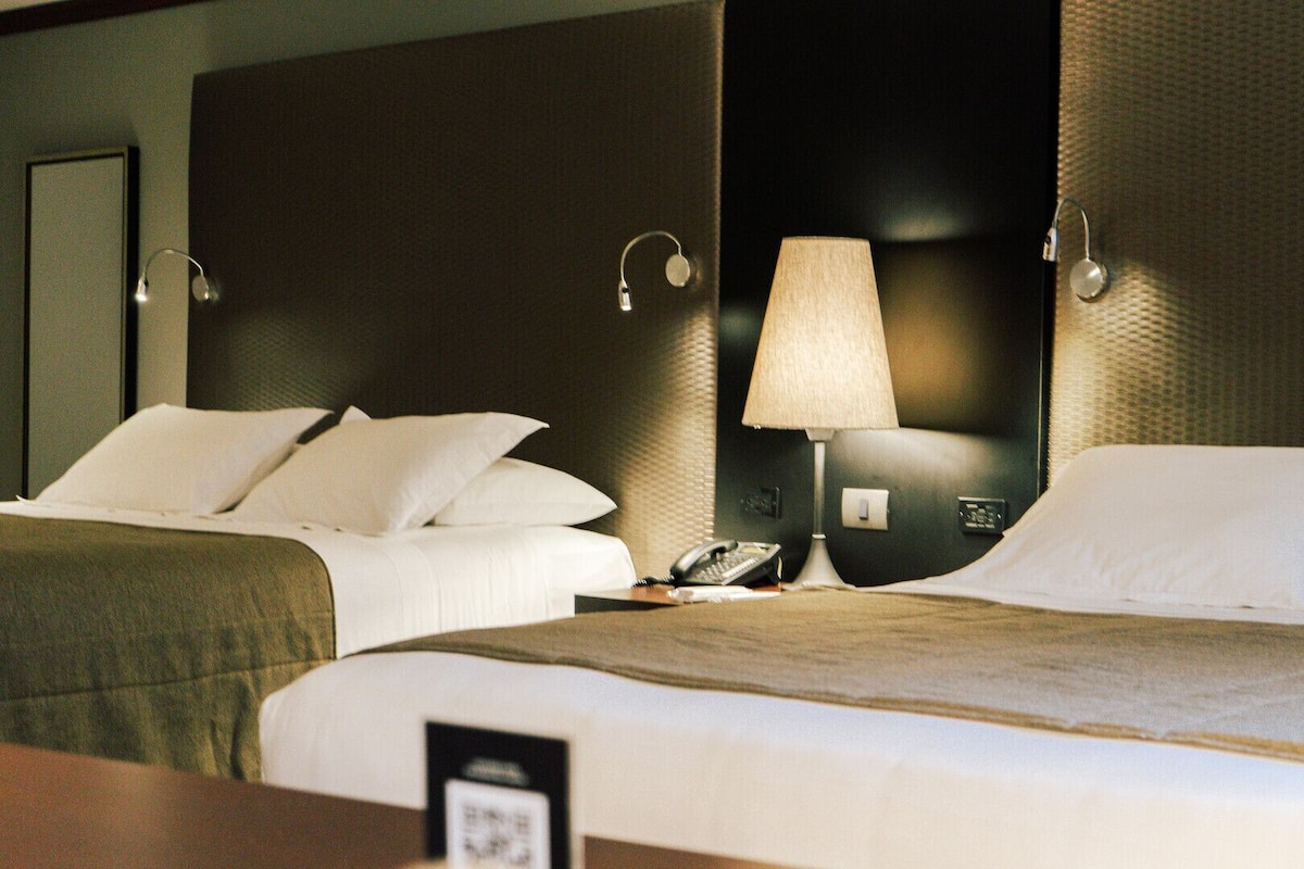 A hotel room with two beds, a bedside lamp, a telephone, and a wall-mounted light fixture.