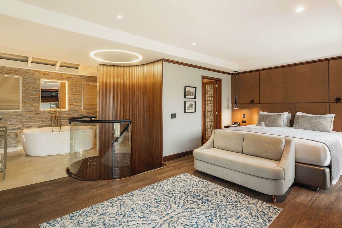 A modern bedroom with a large bed, a glass-enclosed bathtub, and a wooden panel wall.