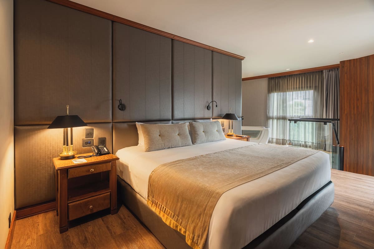 A hotel room with a large bed, a nightstand with a lamp, a telephone, and a wardrobe.