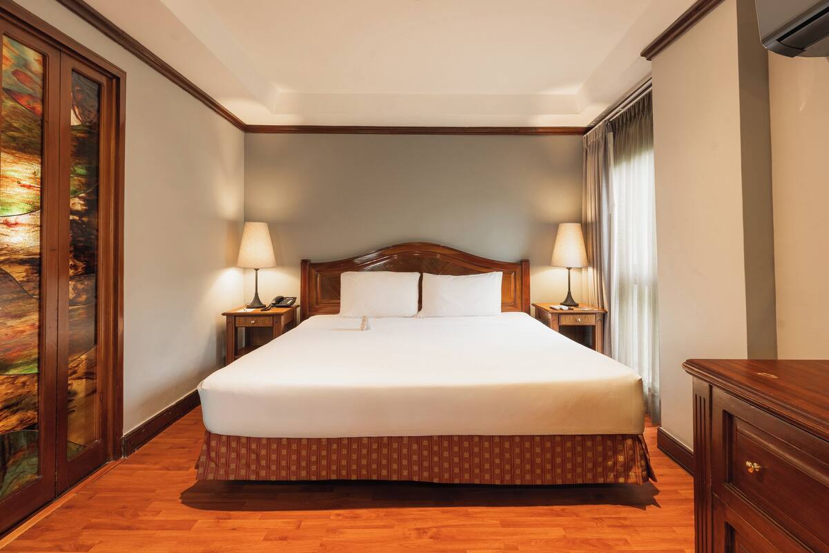 A hotel room with a large bed, two bedside lamps, a wooden headboard, and a painting on the left wall.