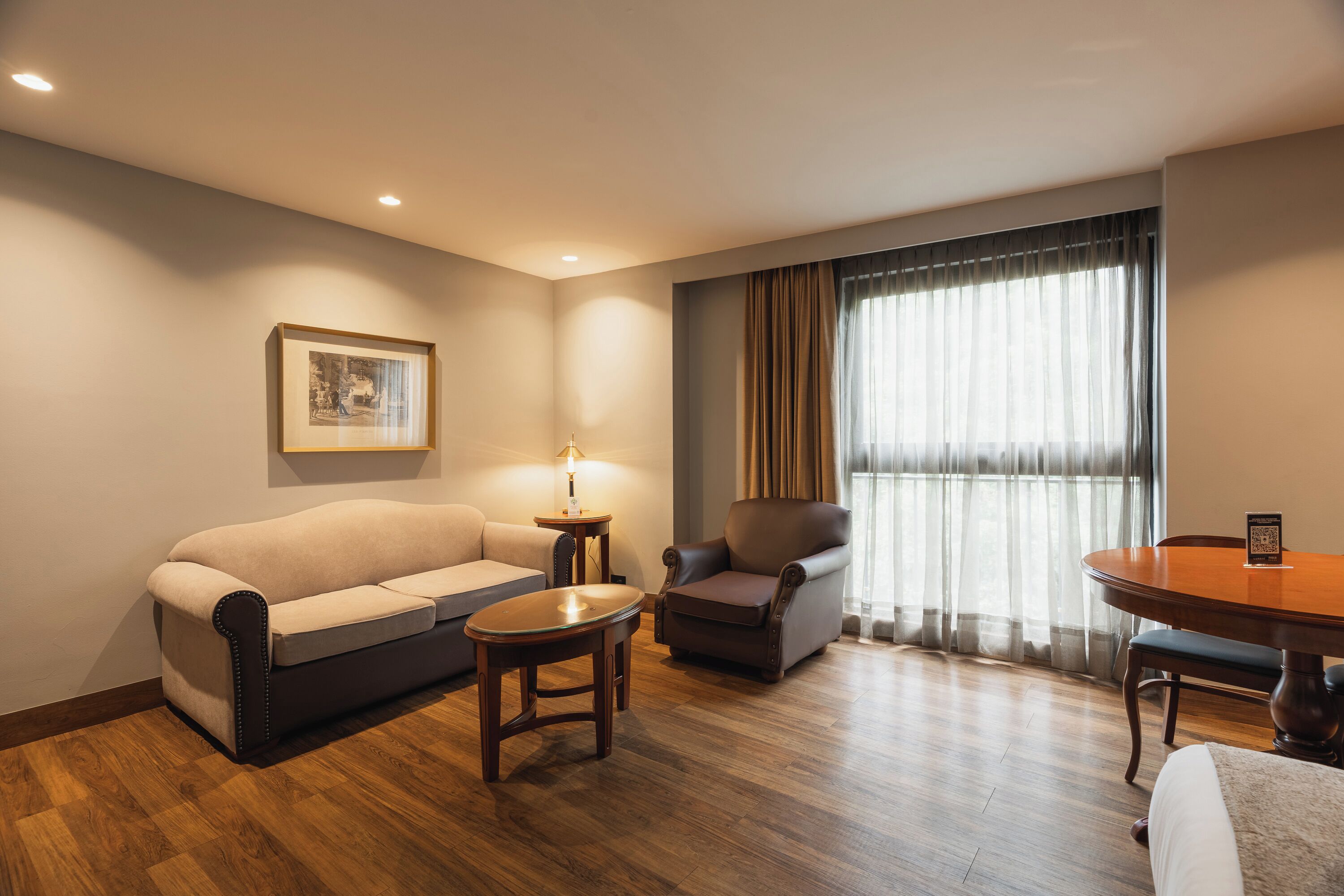 Habitación de hotel con sofá, sillón, mesita y mesa de comedor.