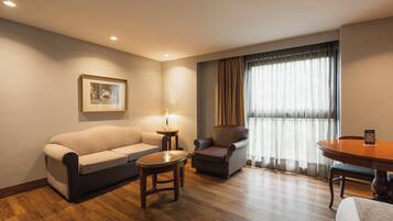 Habitación de hotel con sofá, sillón, mesita y mesa de comedor.