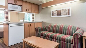A compact living space with a kitchenette, a striped sofa, and a small table. - Microtel Inn & Suites by Wyndham West Chester (West Chester)