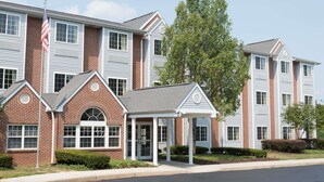 A multi-story building with a brick facade and white trim, featuring a covered entrance and a flagpole. - Microtel Inn & Suites by Wyndham West Chester (West Chester)