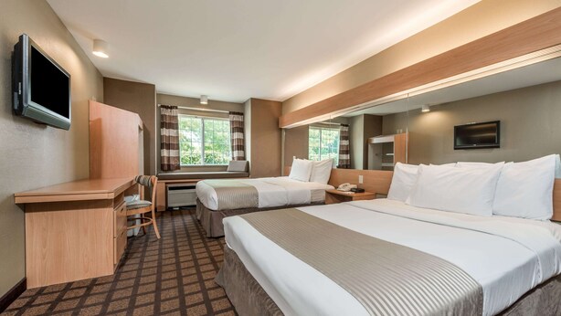 A hotel room with a large bed, a desk, a chair, a TV, and a window with curtains. - Microtel Inn & Suites by Wyndham West Chester (West Chester)