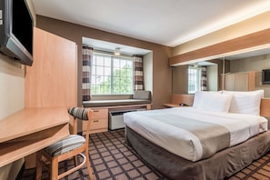 Une chambre d’hôtel comprenant un lit, un bureau, une chaise, une télévision, une fenêtre avec des rideaux et un miroir.