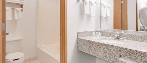 Une salle de bain avec des toilettes blanches, une douche, un lavabo doté d’un plan de travail en granit et un miroir.