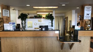 Un mostrador de recepción de hotel con encimera de madera, una computadora Dell y un cartel que indica los horarios del desayuno.