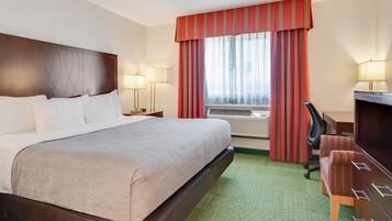 A hotel room with a large bed, a desk, a chair, and a window with curtains.