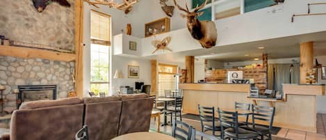 A spacious lounge area with a stone fireplace, a brown leather sofa, and a dining table with chairs.