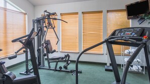 Un gimnasio con equipo de ejercicio, una cinta de correr y un televisor montado en la pared.