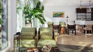 A spacious living room with a large window, green upholstered chairs, a wooden coffee table, and a bookshelf. - Hilton Garden Inn Davis Downtown (Davis)