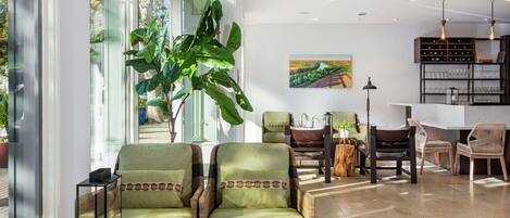 Un salón amplio con un gran ventanal, sillones tapizados en verde, una mesa de centro de madera y una estantería.
