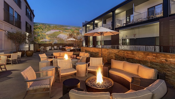 An outdoor seating area with wicker furniture, a fire pit, and a view of a vineyard. - Hilton Garden Inn Davis Downtown (Davis)