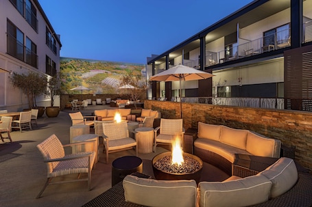 An outdoor seating area with wicker furniture, a fire pit, and a view of a vineyard.