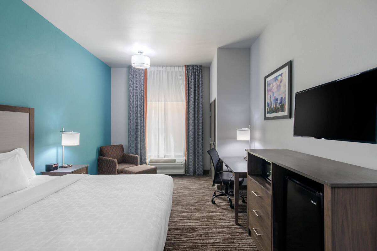 A hotel room with a bed, desk, chair, and a flat-screen TV.