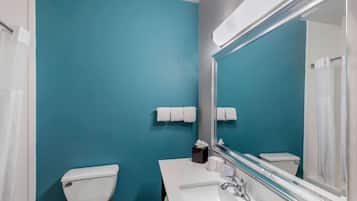 Un baño con lavamanos blanco, un espejo y un inodoro frente a una pared verde azulado.